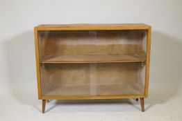 A mid century teak open bookcase with sliding glass doors, raised on splay supports, 36" x 12" x 29"