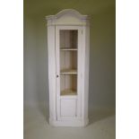 A white painted corner display cabinet with arch top and canted sides, with single glazed door