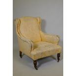 A Victorian wing back easy chair, raised on turned supports with brass and ceramic castors