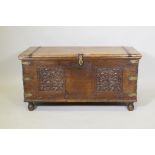 A C19th Eastern teak coffer with bronze mounts and iron strapped top, and carved panels to the