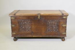 A C19th Eastern teak coffer with bronze mounts and iron strapped top, and carved panels to the