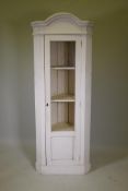 A white painted corner display cabinet with arch top and canted sides, with single glazed door