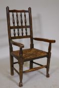 A C19th child's spindle back Lancashire elbow chair with rush seat, raised on turned supports with