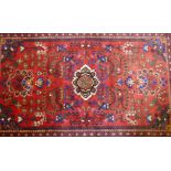 An oriental Hamadan wool carpet with medallion design on a red field, 82" x 54"