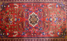 An oriental Hamadan wool carpet with medallion design on a red field, 82" x 54"