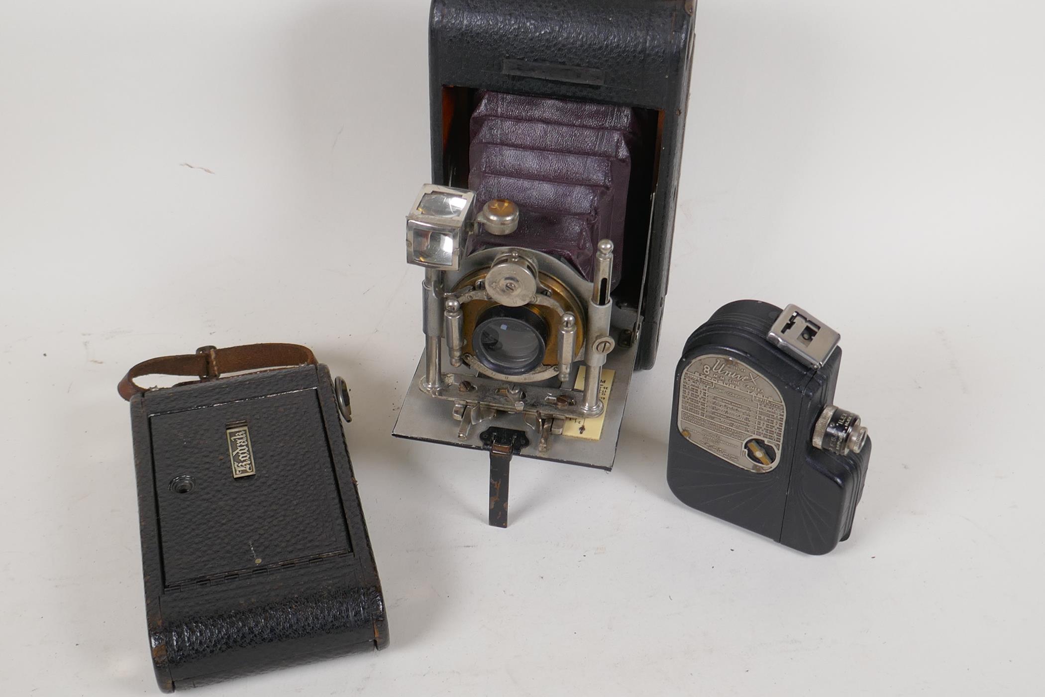 Three vintage cameras, a Bausch and Lamb folding camera (back missing), a Kodak Junior, and a Univex