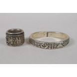 A Chinese white metal bangle with raised decoration of the eight Buddhist treasures, and a white