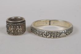 A Chinese white metal bangle with raised decoration of the eight Buddhist treasures, and a white