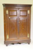 A Georgian oak corner cupboard, the dentil cornice over two doors with fielded panels opening to