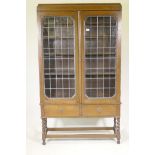 An oak bookcase, the upper section with two leaded light doors, the base with two drawers, raised on