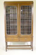 An oak bookcase, the upper section with two leaded light doors, the base with two drawers, raised on