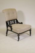 A Victorian Aesthetic style ebonised nursing chair with pierced spindle back, raised on tapering