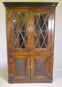 An antique oak corner cabinet with two glazed doors over two doors with carved panels, adapted,