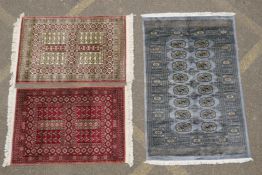 A blue / grey ground Bokhara carpet and two other smaller rugs with red and ivory grounds, largest