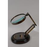 A brass framed desk top magnifying glass on a wooden base, lens 5" diameter