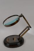 A brass framed desk top magnifying glass on a wooden base, lens 5" diameter