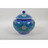 A blue and white porcelain jar and cover with scrolling red lotus flower decoration on an