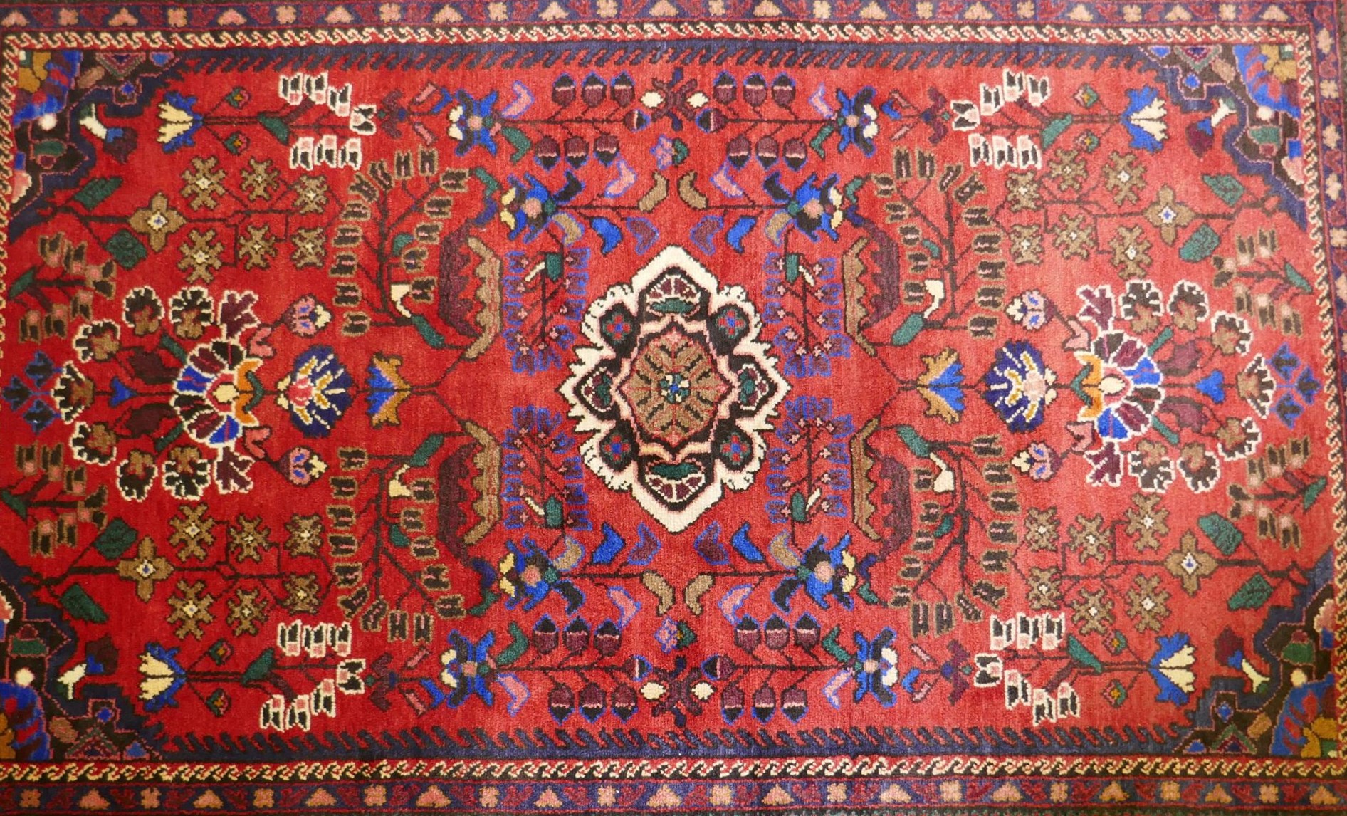An oriental Hamadan wool carpet with medallion design on a red field, 82" x 54"