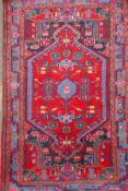 A Persian red ground wool rug with a multicolour geometric medallion design, 33" x 52"