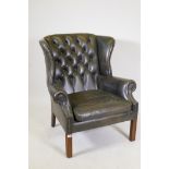 A Georgian style button back green leather wing armchair