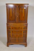 A bow front yew wood cocktail cabinet, two cupboards opening to reveal a mirrored back, over a