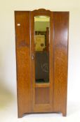 A small Art Deco oak wardrobe with single mirrored door and raised decoration, and raised on