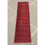 A Persian rich red ground wool runner with a floral medallion design and black borders, 33" x 116"