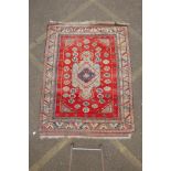 A Persian red ground wool carpet with a geometric medallion design and blue borders, 58" x 75"