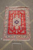 A Persian red ground wool carpet with a geometric medallion design and blue borders, 58" x 75"