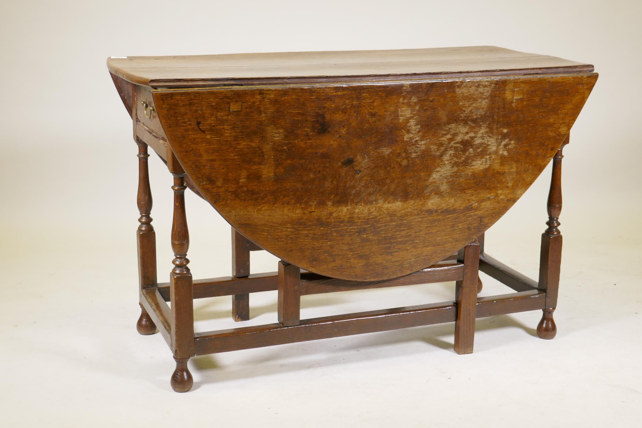 An C18th oak gateleg drop leaf table with single long drawer, raised on turned baluster shaped - Image 2 of 5
