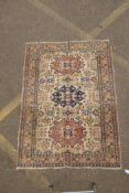 An antique Persian cream ground wool rug decorated with three central geometric medallions and faded