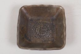 A Chinese square section white metal dish cast with dragons and symbols, 4 character mark to base,