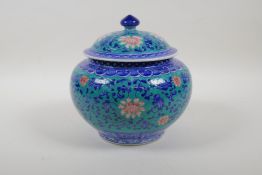 A blue and white porcelain jar and cover with scrolling red lotus flower decoration on an