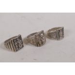 A Chinese white metal ring with raised decoration of Buddha flanked by two censers, another with a