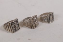 A Chinese white metal ring with raised decoration of Buddha flanked by two censers, another with a