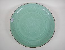 A Chinese celadon green glazed ceramic charger with raised dragon decoration, blue seal mark to