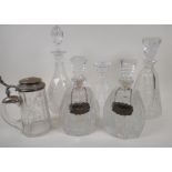 Five cut glass decanters, two with hallmarked silver spirit labels, and an engraved faceted glass