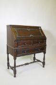 A Jacobean style carved oak bureau with fall front over two short and one long drawer, raised on
