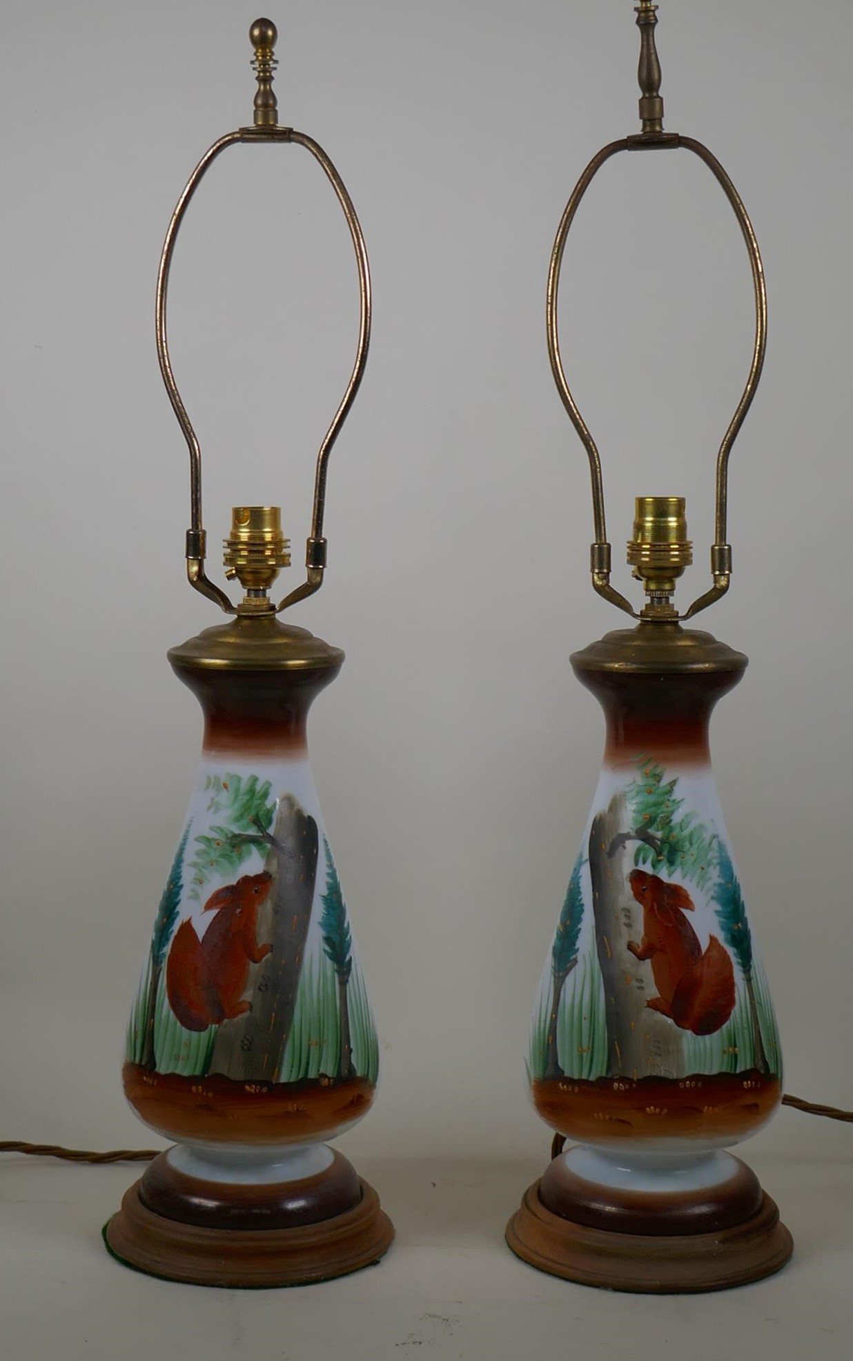 A pair of opaline glass table lamps with hand painted decoration of red squirrels amongst pine