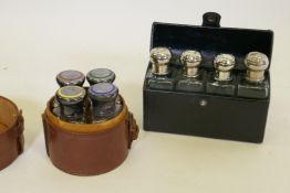 A leather case vanity set comprising four shaped bottles, the silver tops with enamel decoration,