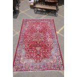 A vintage fine woven Persian Isfahan wool red ground carpet with blue borders, worn, 210cm x 318cm