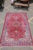 A vintage fine woven Persian Isfahan wool red ground carpet with blue borders, worn, 210cm x 318cm