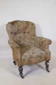 A Victorian easy chair with shaped back and scroll arms, raised on turned supports with brass