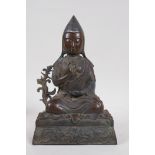 A Tibetan bronze figure of Buddha, seated and wearing a pointed cap, impressed with inscription