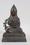 A Tibetan bronze figure of Buddha, seated and wearing a pointed cap, impressed with inscription