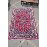 A red ground Persian Mashat carpet with a traditional floral medallion design, signed weaver,