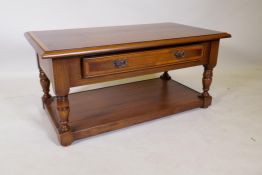 An oak two tier coffee table with cross banded top and single drawer, raised on turned supports, 100