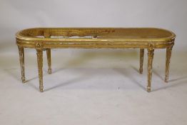 A C19th gilt wood window seat with oval cane top on six fluted supports, cane AF, 45 x 132 x 43cms