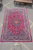 A red ground Persian Mashat carpet with a traditional floral medallion design, signed weaver,