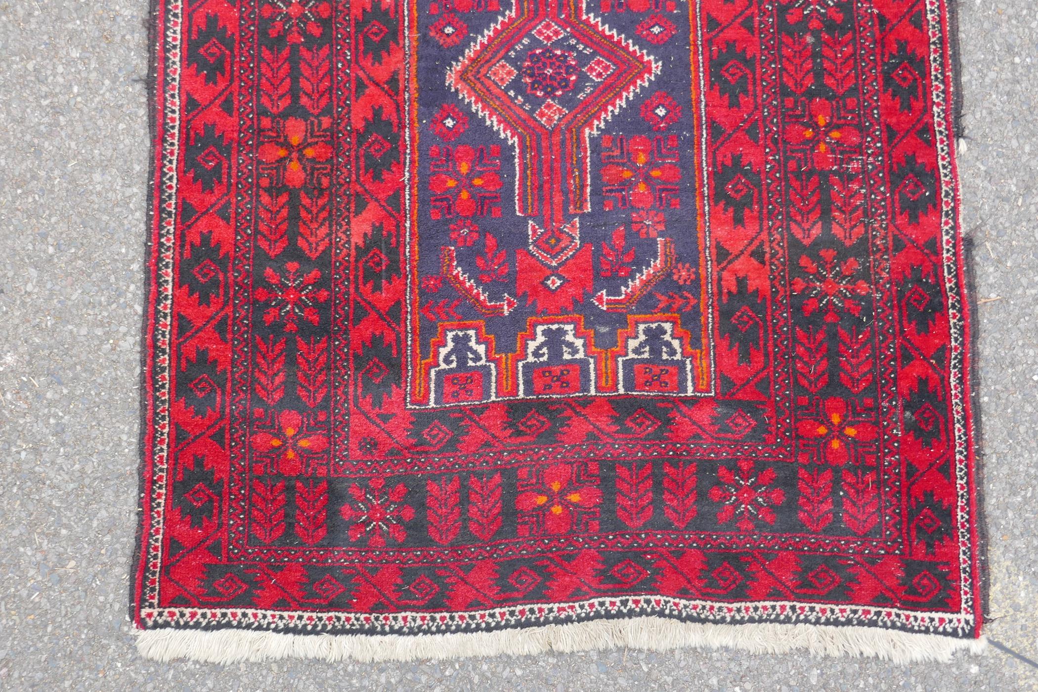 A Turkish deep red ground wool rug, with geometric designs on a central deep blue cartouche, 100 x - Image 2 of 7